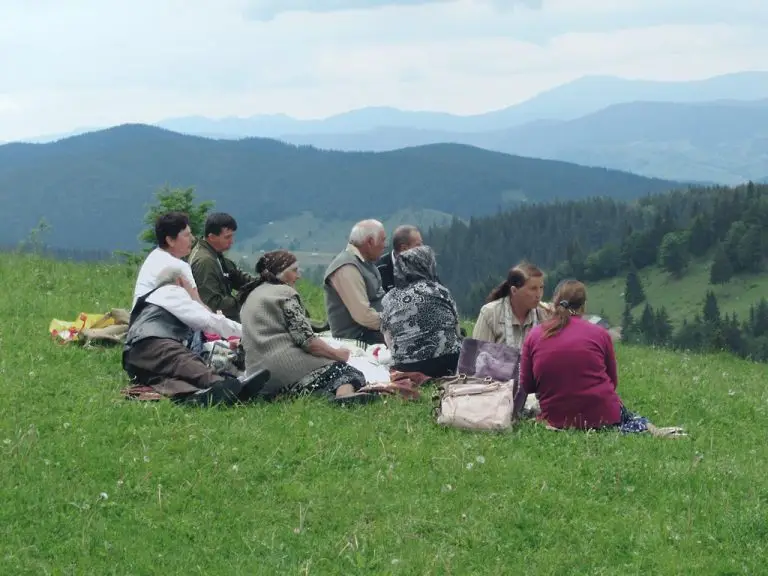 Familie românească luând prânzul împreună pe o pajiște din Bucovina.